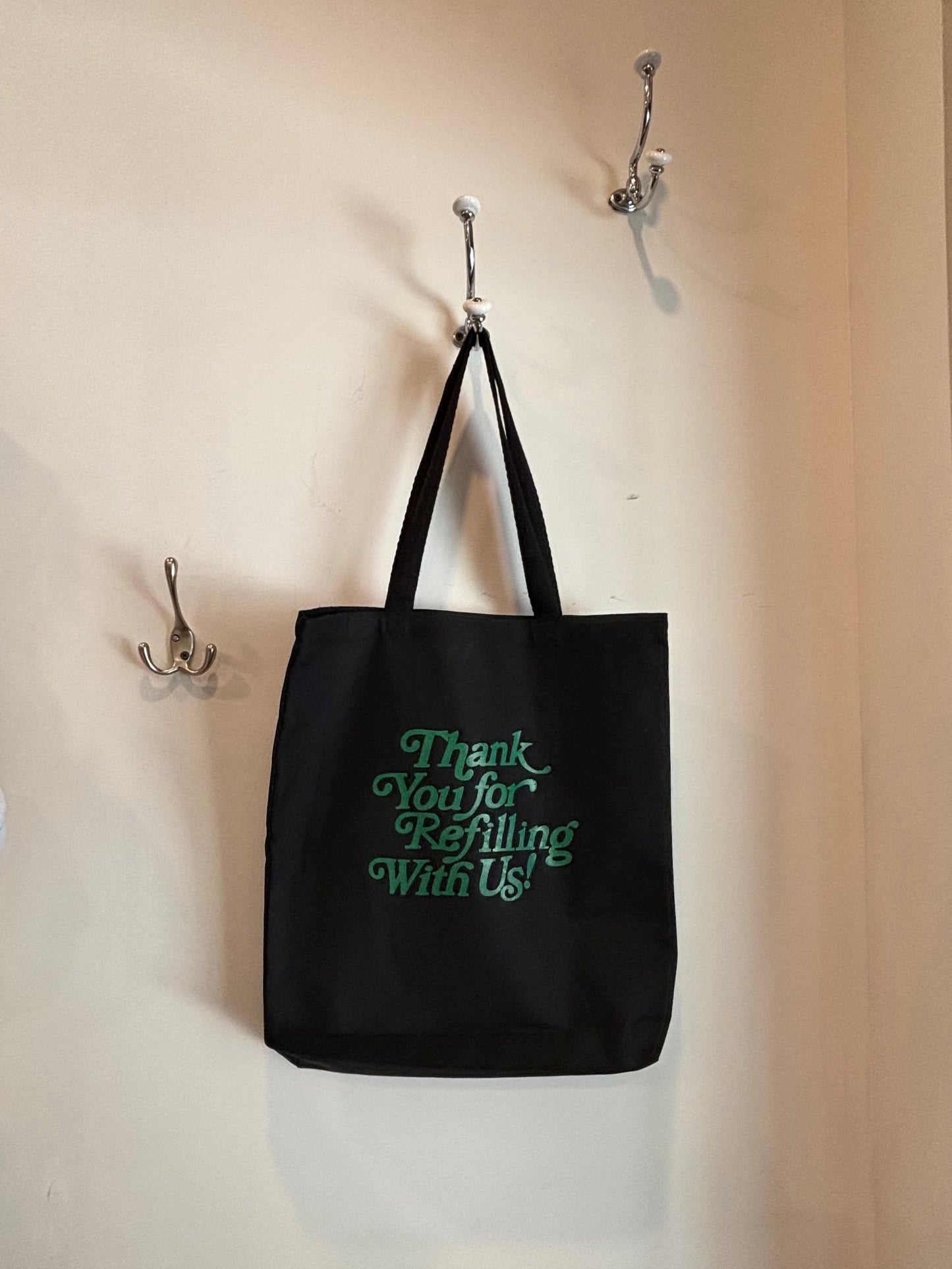 Black tote bag with green text hanging on a wall hook.